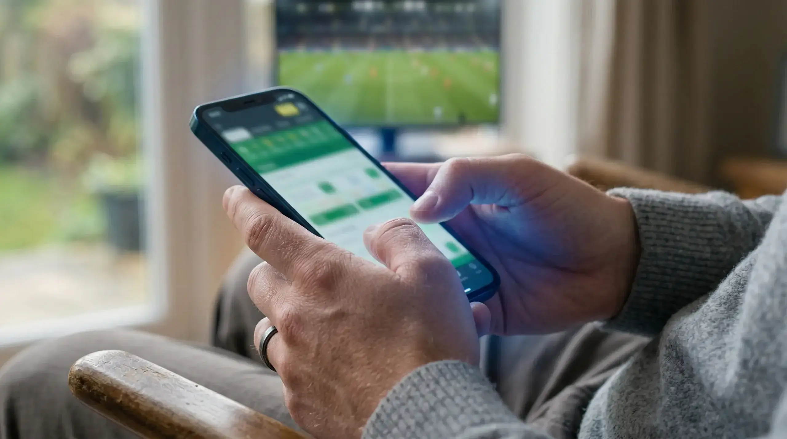 Persoon plaatst een eerste weddenschap op een smartphone met voetbal op de achtergrond